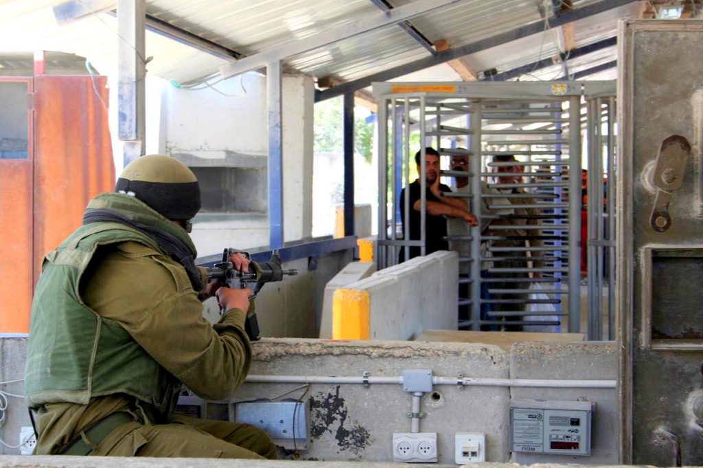 Israeli soldier faces Palestinians waiting at the Huwara checkpoint, at the entrance to Nablus, 12 June 2006.